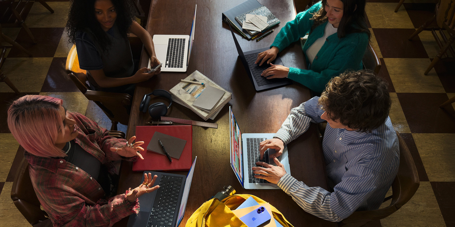 Trois étudiantes et un étudiant sont autour d’une table, avec des notes et leurs MacBook ouverts devant eux.