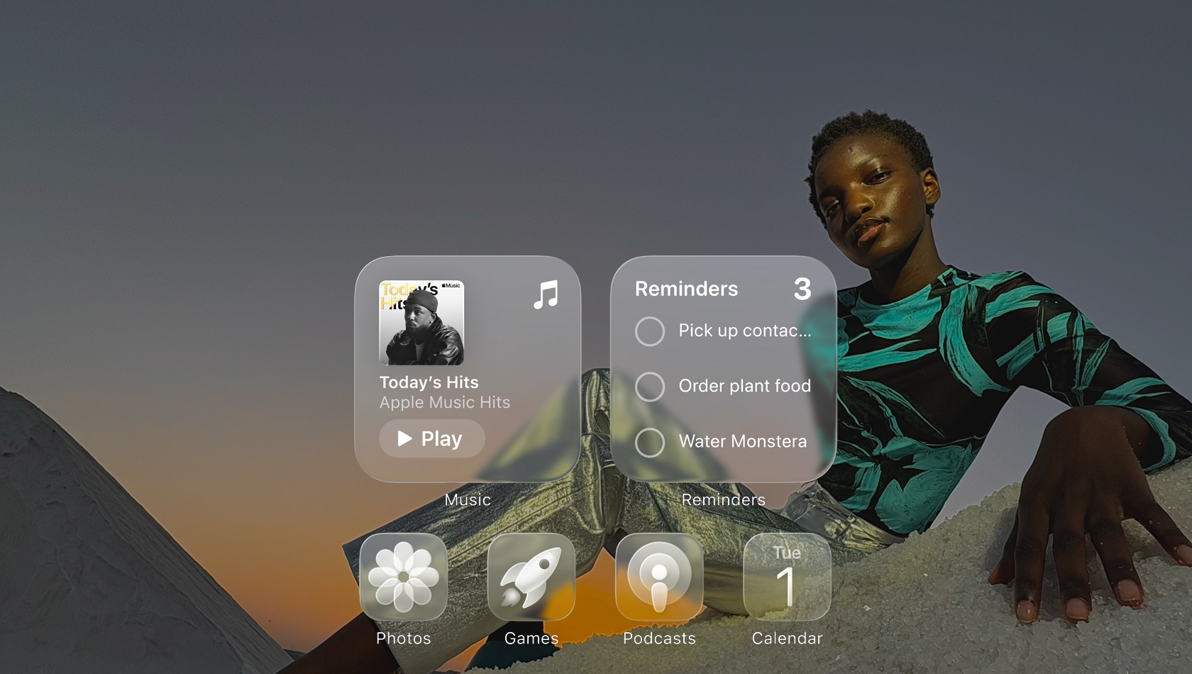 Wyświetlacz Liquid Glass z przejrzystymi ikonami aplikacji – Apple Music, Przypomnienia, Zdjęcia, Gry, Podcasty i FaceTime – które subtelnie rozmywają obraz tapety