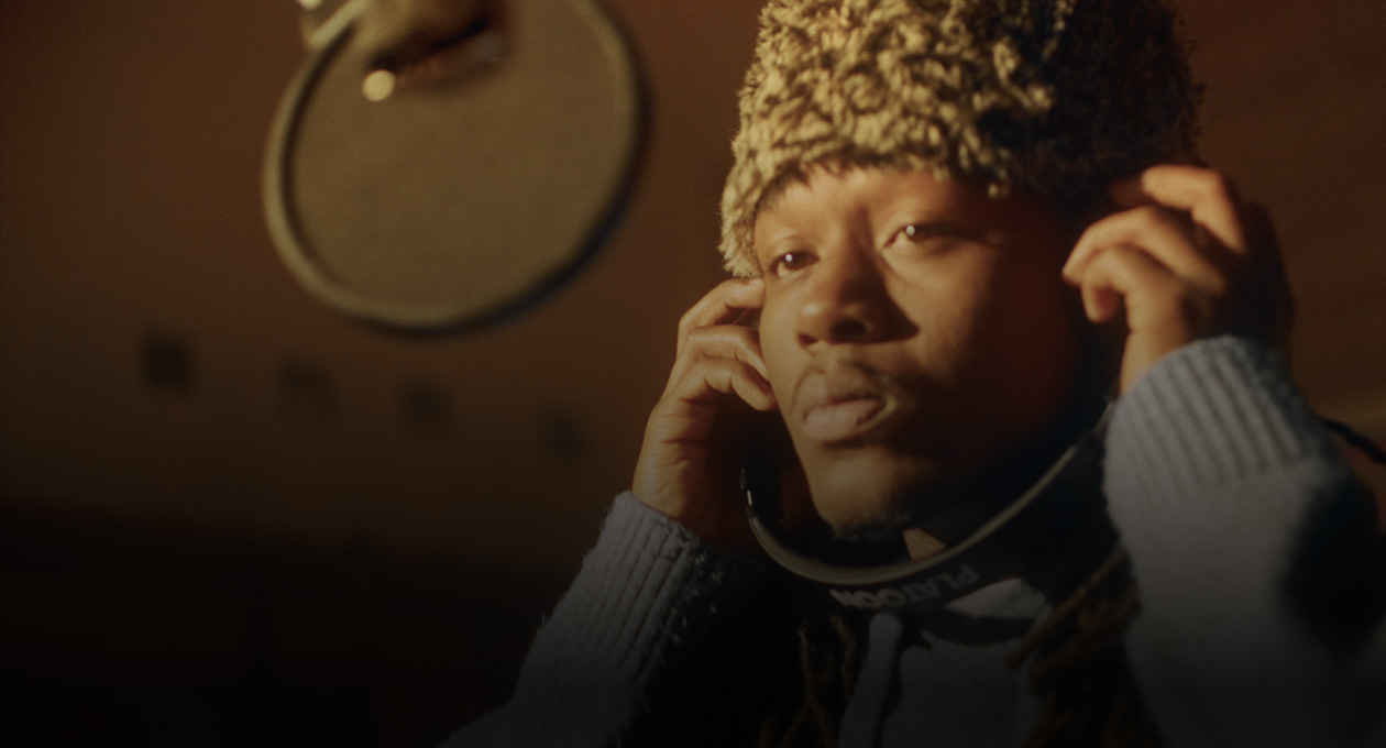 صورة لمغني الراب كيدو كاي في استوديو موسيقي، وهو يقف أمام ميكروفون التسجيل ويستمع عبر سماعات الرأس