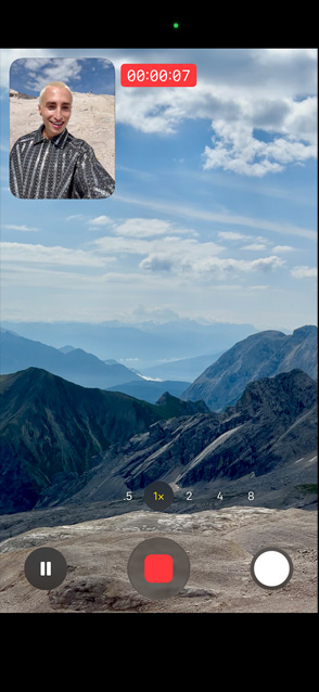 Henkilö esittelee kaksoisotto-videokuvausta kuvaamalla itseään etukameralla ja samanaikaisesti kuvaamalla luonnonkauniita vuoria takakameralla